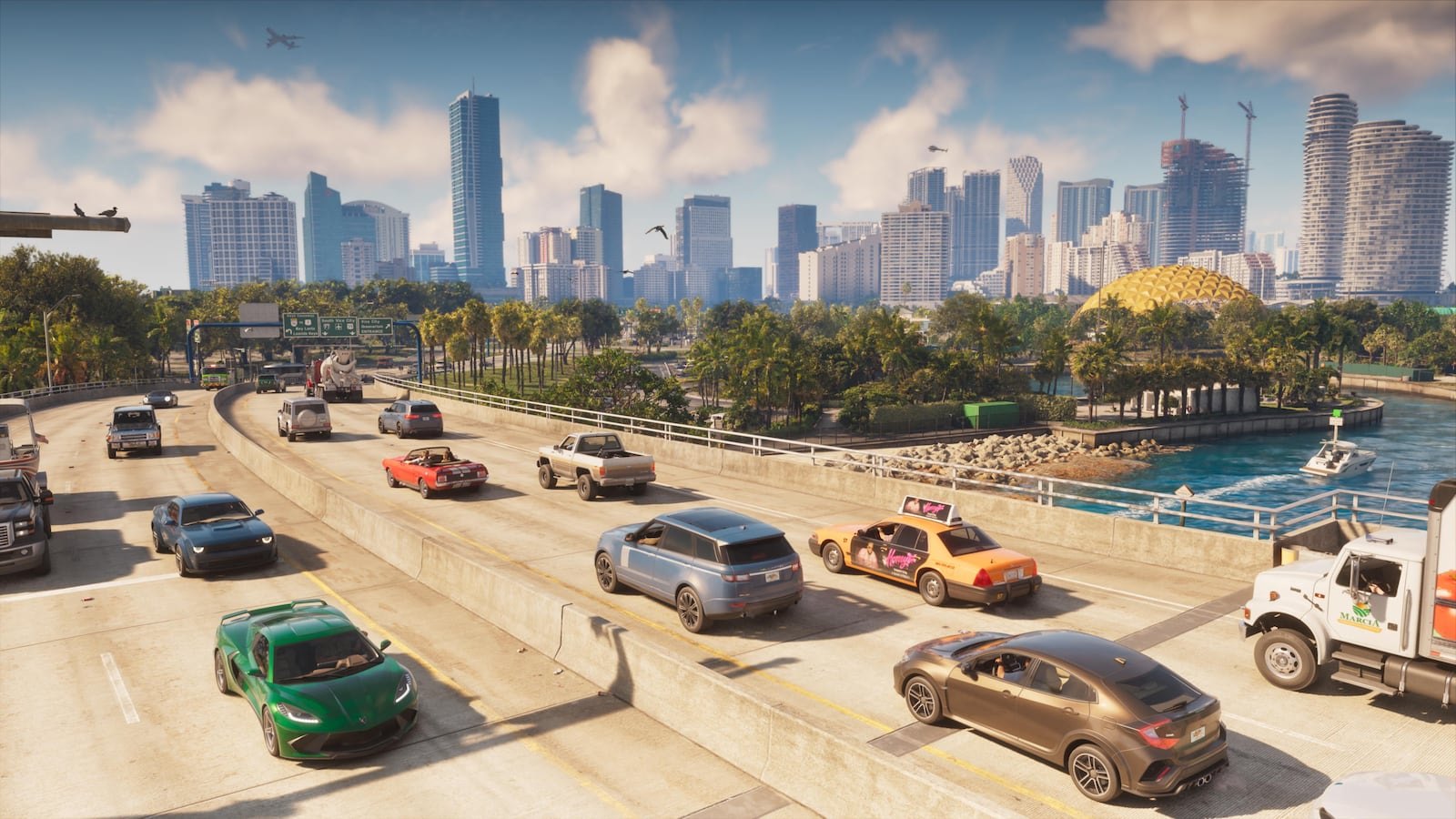 A busy multi-lane highway filled with various vehicles passes alongside a waterway with a modern city skyline visible in the background.