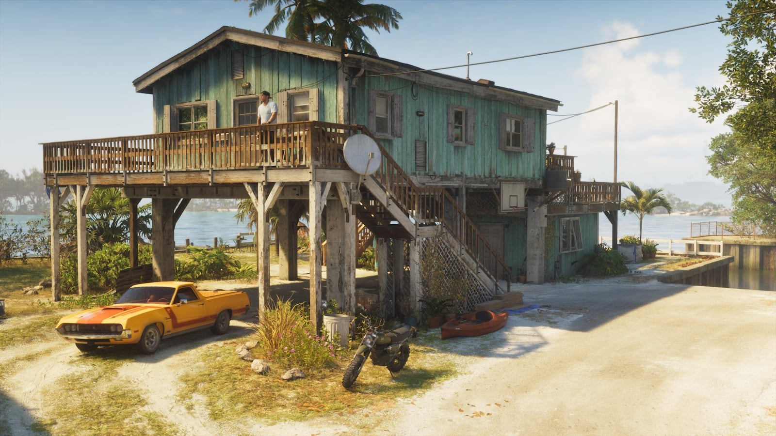 A weathered turquoise stilted wooden house near the water with a yellow muscle car, motorcycle, and kayaks visible outside under sunny skies.